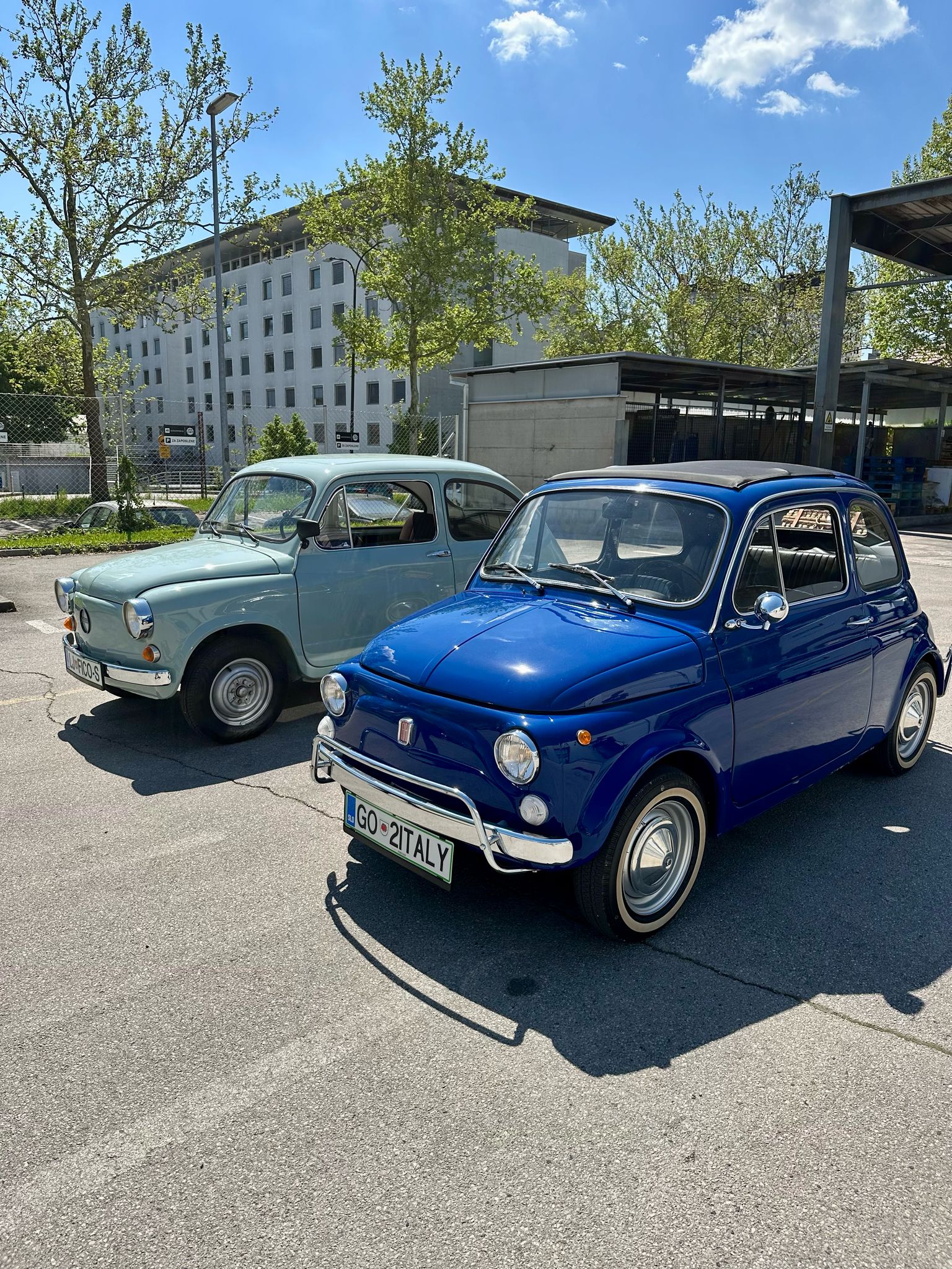 Luigi Aperitivo – klasični modri Fiat 500 parkiran ob sodobnih avtomobilih, simbol pristne osebnosti in italijanskega šarma.